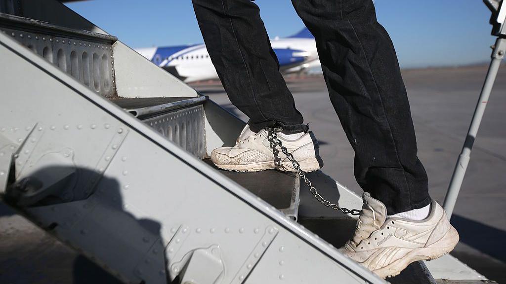 A Honduran immigration detainee, his feet shackled and shoes laceless as a security precaution, boards a deportation flight to Honduras