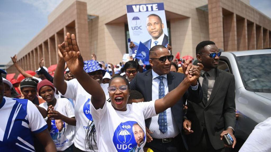 A smiling UDC supporter holds her hands in the air as she greets party leader Duma Boko.