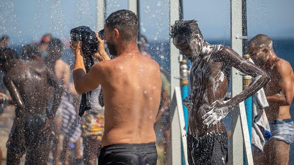 Migrants use outdoor showers at a beach encampment in Ceuta, Spain, 25 August 2026