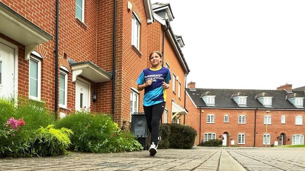 Daisy-Grace Lynch running along a street pavement wearing a blue Parkinson's UK t-shirt