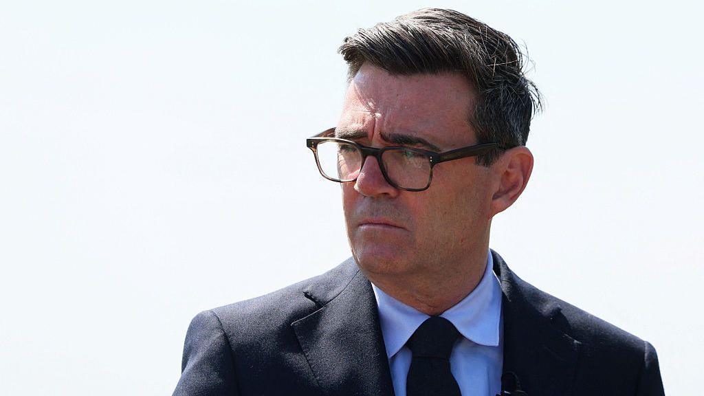 Andy Burnham, wearing a blacksuit and black glasses