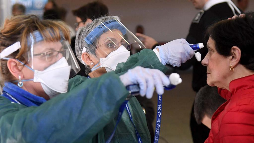 A healthcare professional wearing protective suit and healthcare mask checks the temperature on incomnig people at the entrance of the Maugeri hospital in Pavia, northen Italy, 04 March 2020