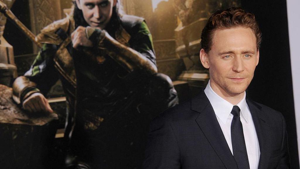 Tom Hiddleston with his character's image Loki behind him.