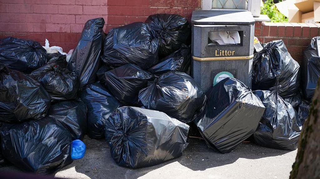 Black plastic bin bags crowd a street.
