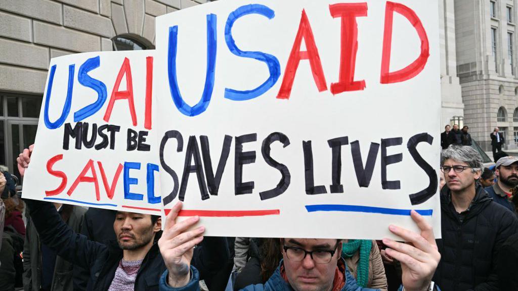 People protest outside of the headquarters for USAID before congressional Democrats hold a news conference in Washington DC on 3 February 2025. They are holding signs that say: "USAID must be saved" and "USAID saves lives".