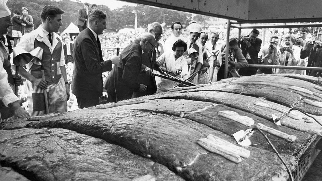 A black and white photograph of a 650 sq ft pie being cut into by men in suits