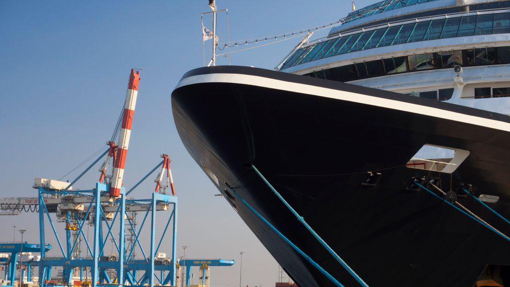 The black hull of a cruise liner, with blue cranes in the background.