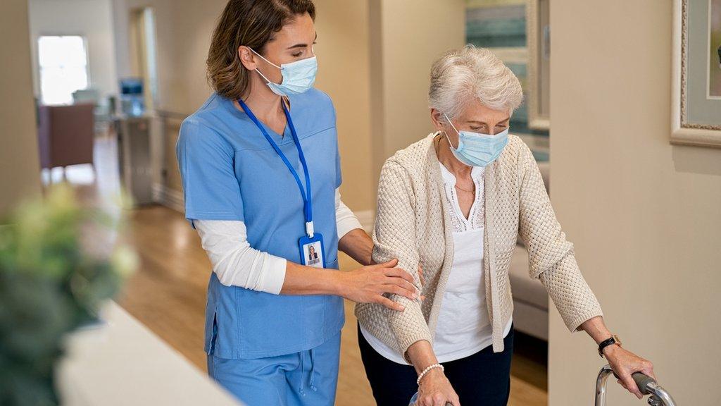 Woman wearing mask helps older woman with walking frame