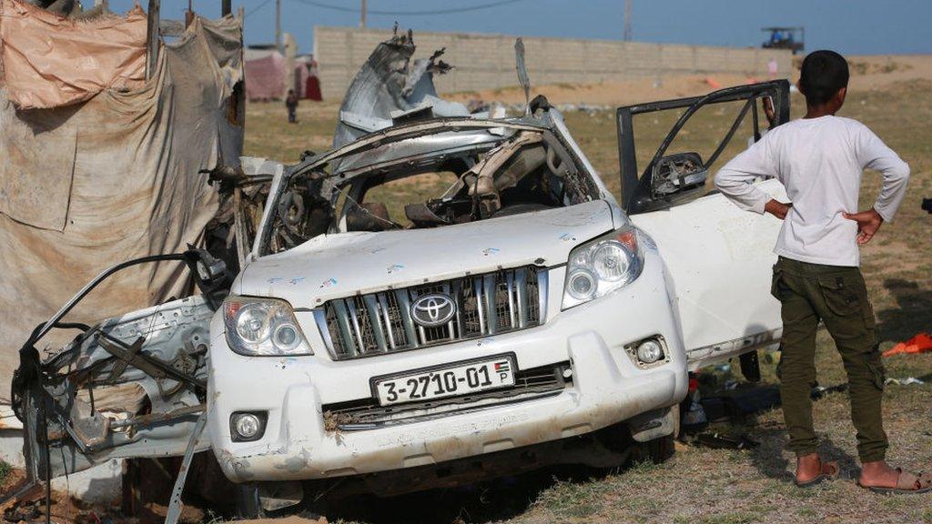 People gather around the carcass of a car used by US-based aid group World Central Kitchen, that was hit by an Israeli strike the previous day in Deir al-Balah in the central Gaza Strip on April 2, 2024,