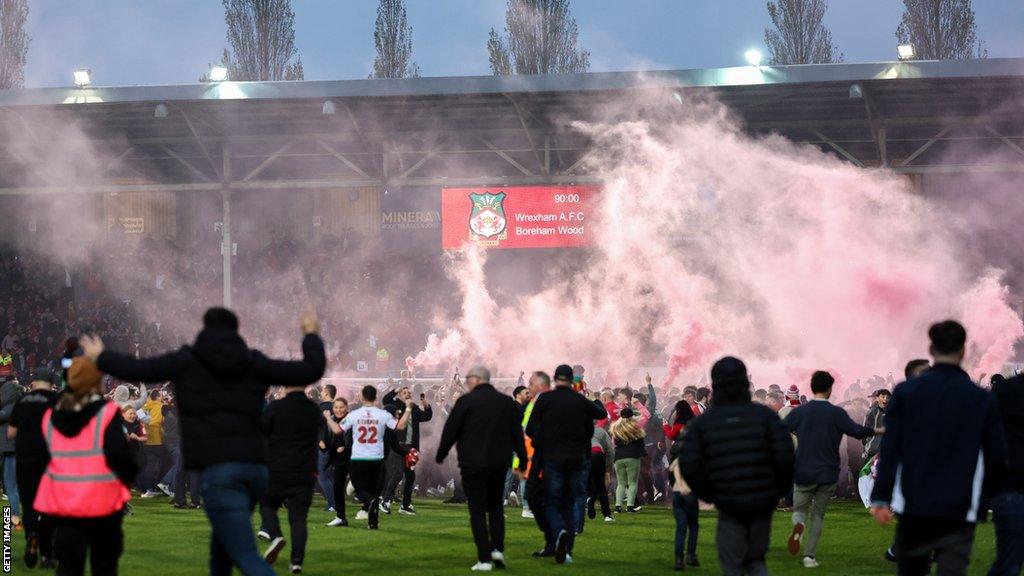 Wrexham fans celebrate on the Racecourse pitch after they clinched promotion by beating Boreham Wood in April