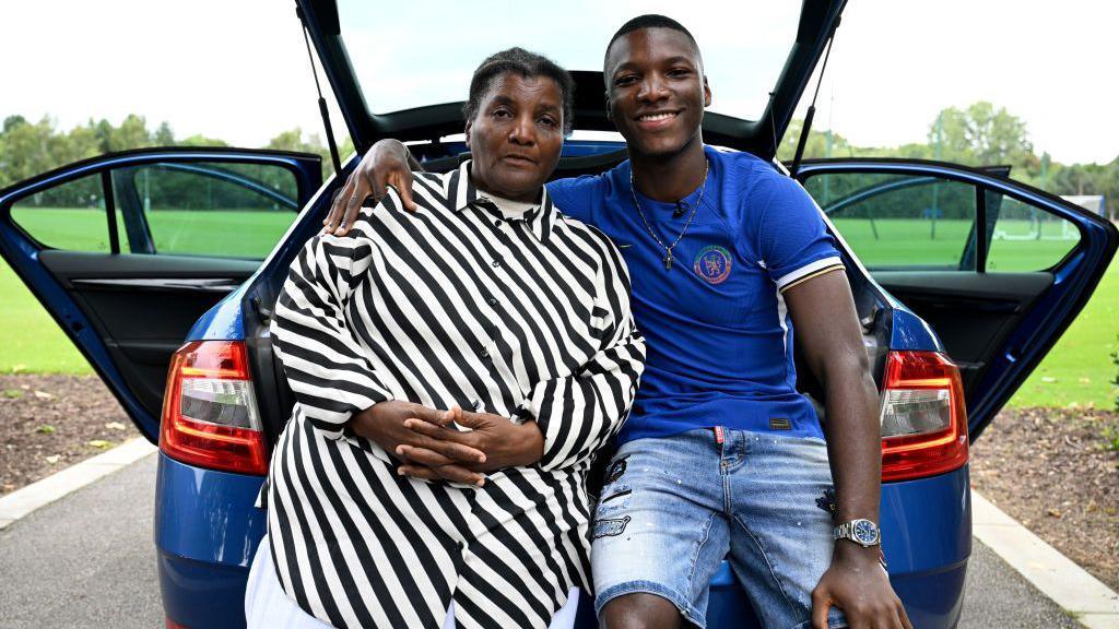 Moises Caicedo and his mother Carmen sit on the boot of car