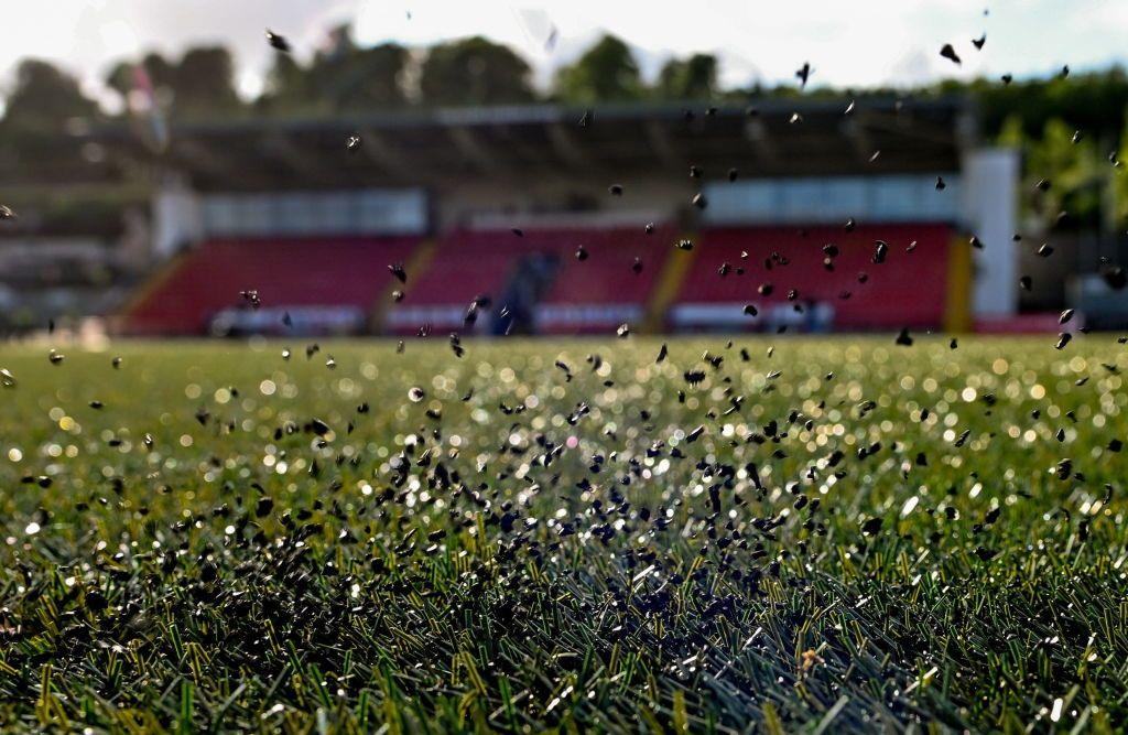 Black rubber crumbs hit bounce up from the ground after the ball hits the turf on an artificial football pitch.