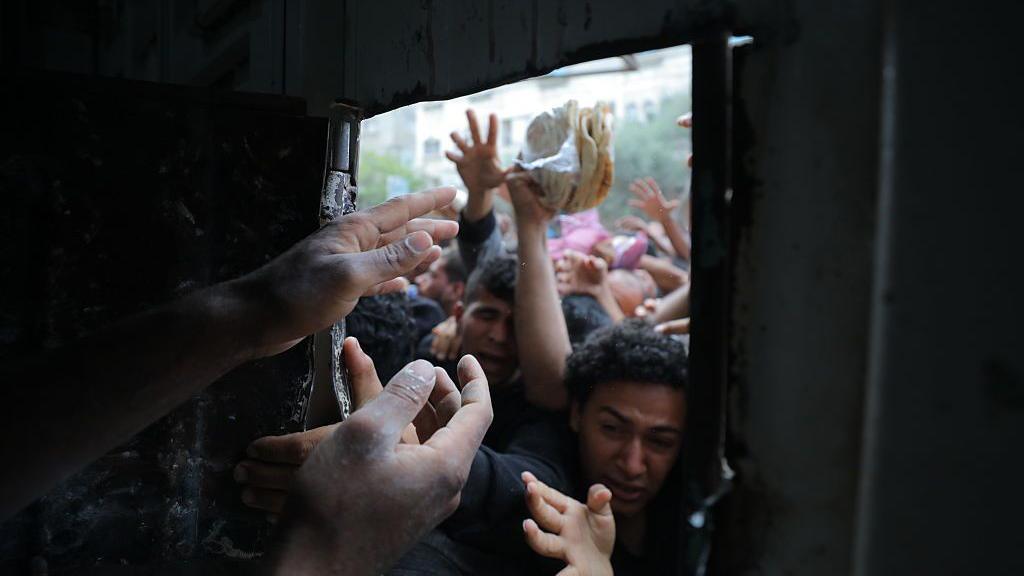 Displaced Palestinians reach through a bakery window as they try to obtain bread after a limited amount of flour entered the Gaza Strip, where humanitarian aid has been severely restricted since March 2, in Nusseirat Refugee Camp, Gaza on May 22, 2025.