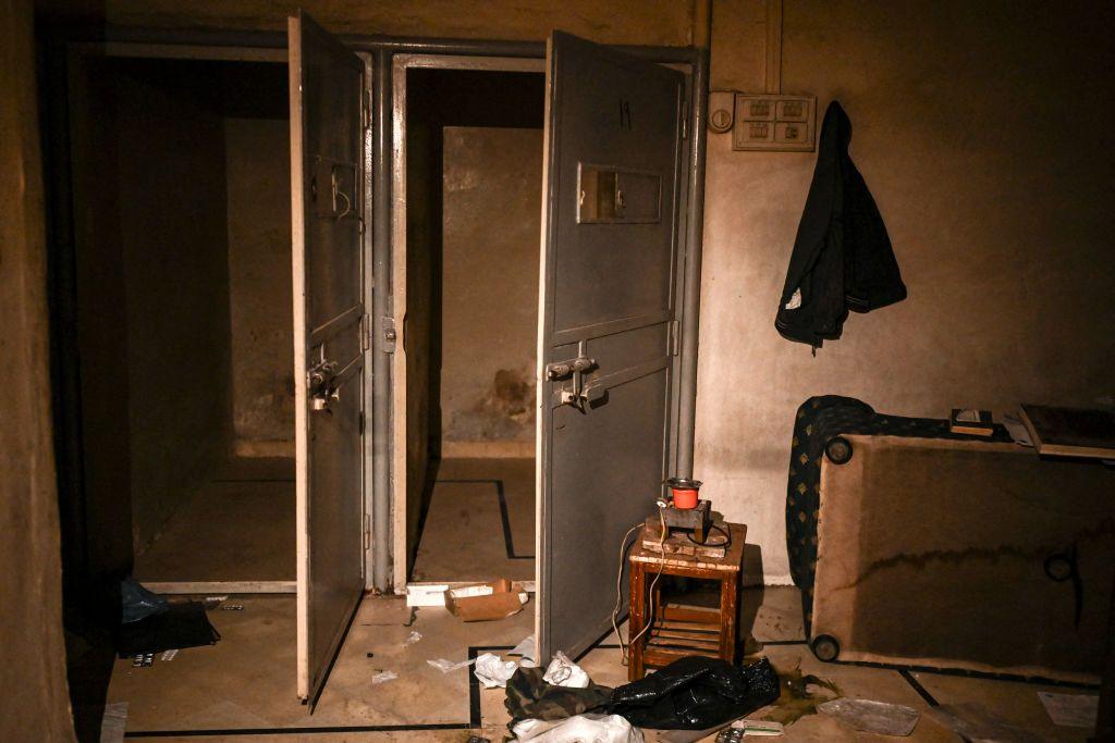 Empty prison cells with bare walls and metal doors with padlocks on them in a basement