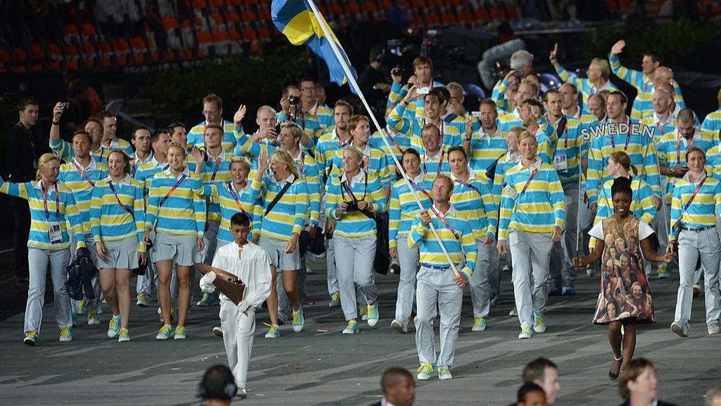 Sweden's flagbearer Rolf-Goran Bengtsson leads the team out at London 2012, with athletes in yellow and blue hooped shirts