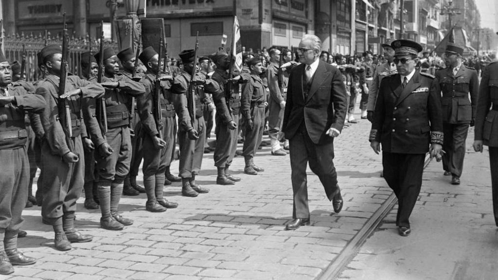 An archive black-and-white archive shot of African troops being inspected by French officials.