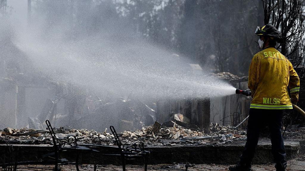 A firefighter sprays water over smoldering rubble
