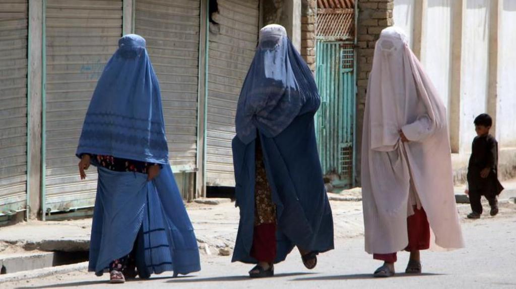 Afghan women wearing burqas travel in the back of a a mini truck 