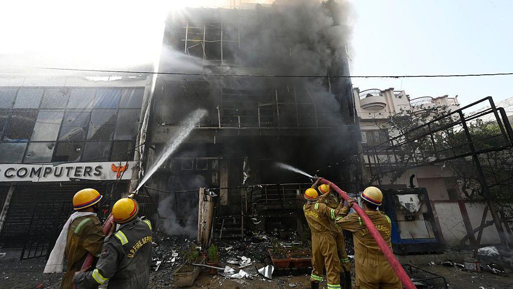 Five firefighters spray water on the burnt building in India's Lucknow. Thick, dark smoke can be seen billowing from the structure.