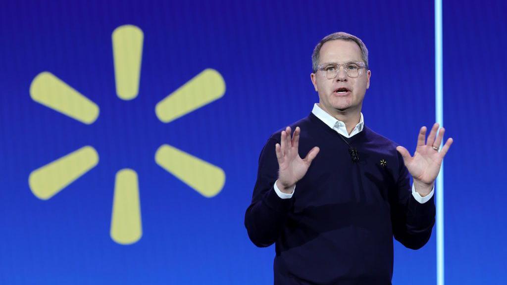 Walmart Inc. President and CEO Doug McMillon in glasses and dark sweater holds up his hands while delivering a keynote address in front of the yellow Walmart logo during CES 2024 at The Venetian Resort Las Vegas on January 9, 2024 in Las Vegas, Nevada.