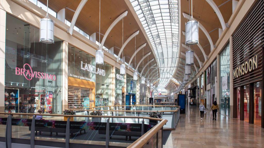 The Grand Arcade in the newer part of the St David's shopping centre in Cardiff, with shops either side of staircases and a glass roof on top of a high celing