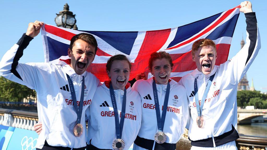 Alex Yee, Georgia Taylor-Brown, Beth Potter and Samuel Dickinson hold up the Union Jack after receiving their mixed relay bronze medals at the Paris Olympics