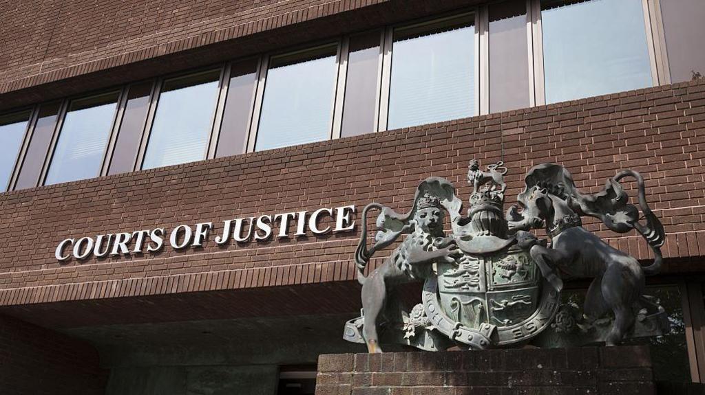 A red brick building with a sign saying "courts of justice" and a copper sculpture of a crest. 