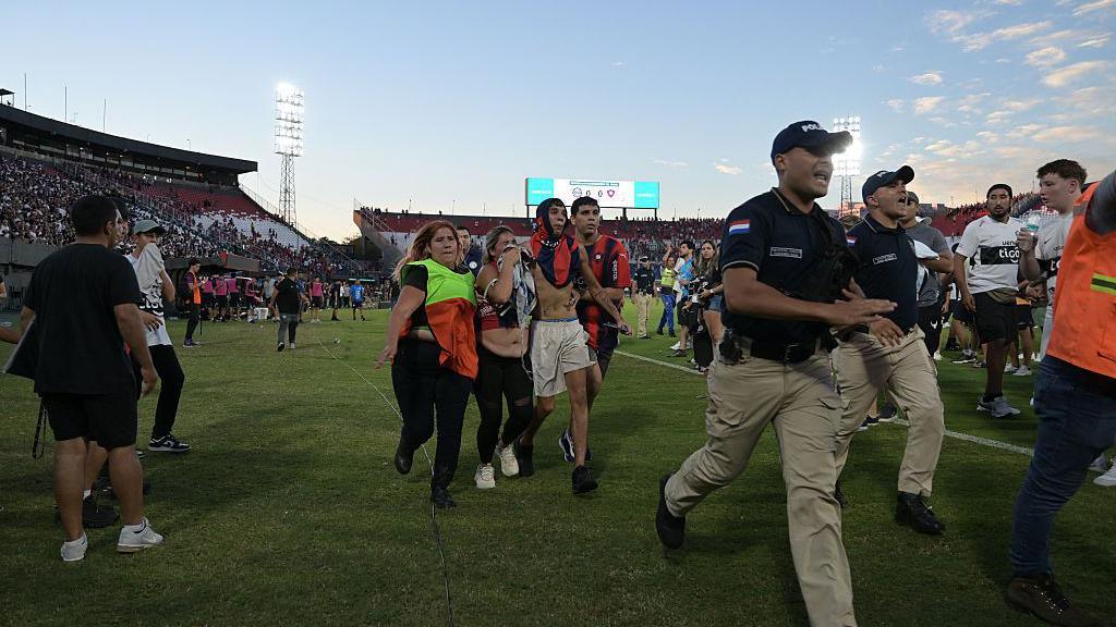 Fans of Cerro Porteno walk on the pitch after clashes with police officers