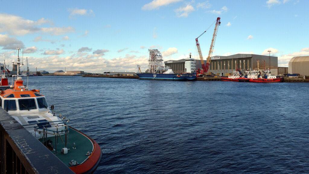 A view over the River Tees of Port Clarence. A number of vessels are docked at the port and a crane towers above them.