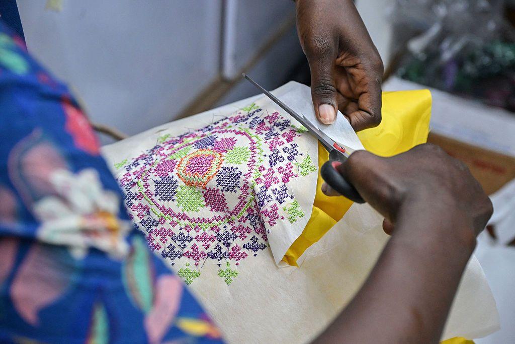 A man cuts around the outside of a colourful motif stitched in threads of multiple colours.