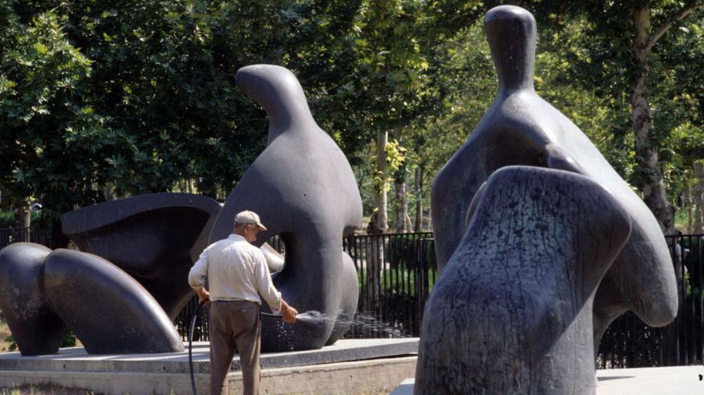 A gardener waters the grass in front of sculptures by British sculptor Henry Moore in the grounds of the Tehran Museum of Contemporary Art, September 1993