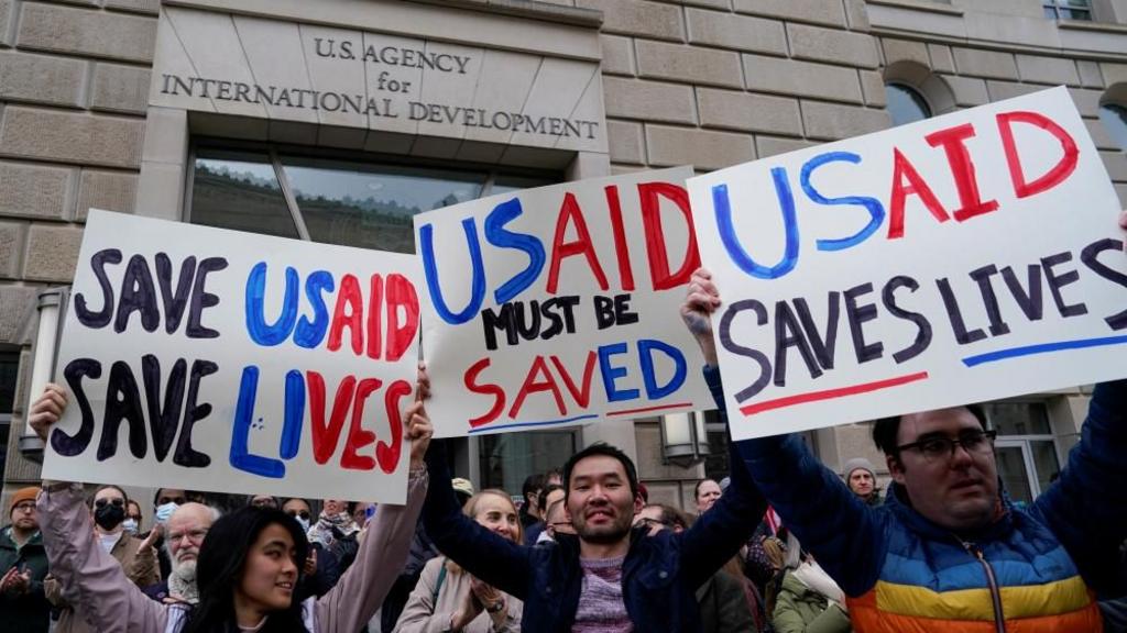 People hold placards, as the USAID building sits closed to employees on Monday