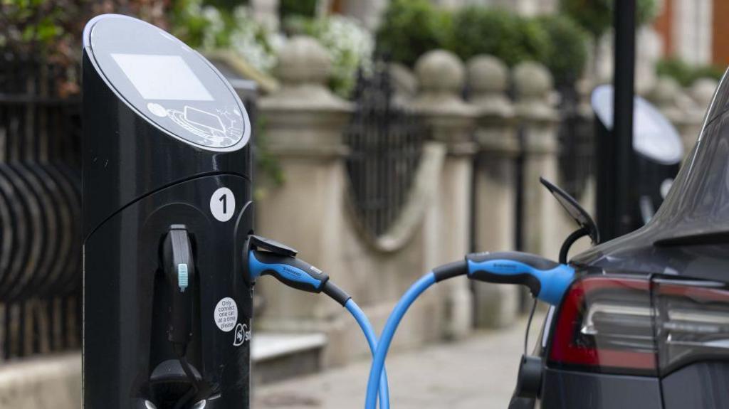 An electric car is charging at a socket next to a pavement.