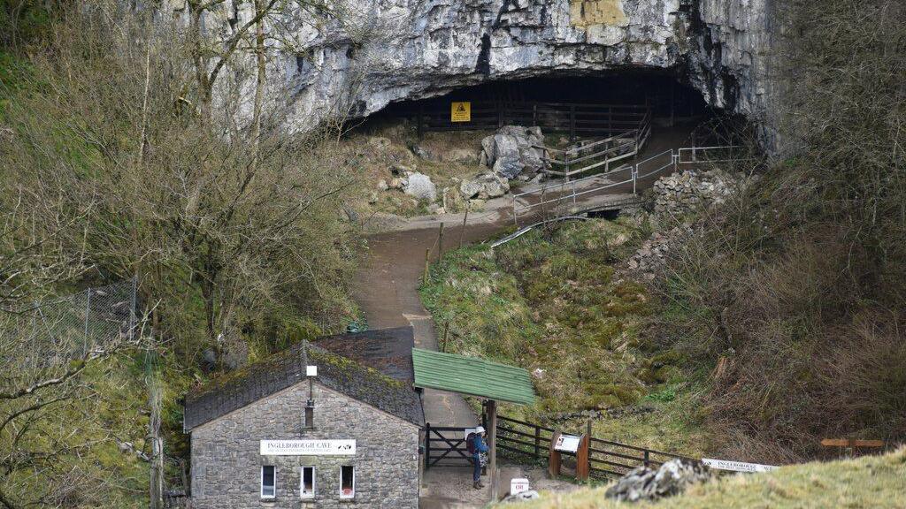 Ingleborough caves seen from above: a stone building and a gate at the end of a path which leads to some stone caves