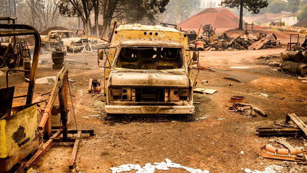 A burned vehicle smolders in the Paynes Creek area of unincorporated Tehama County, California, during the Park fire on July 27, 2024. 