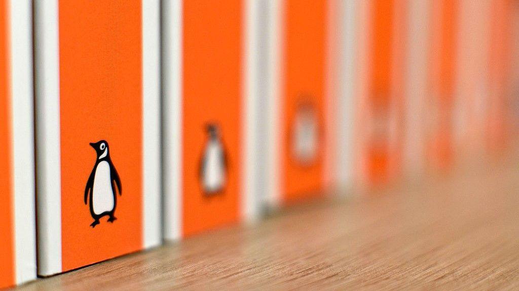 The spines of several orange Penguin paperback books are on a shelf. Only the one nearest the camera is in focus. The Penguin logo can be seen on each.