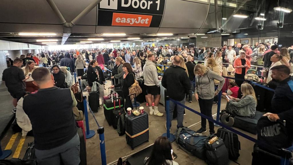 Passengers queue at the Manchester Airport after cancellations from a power outage.