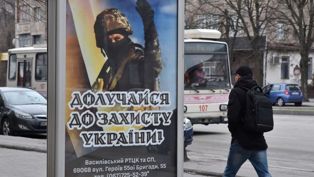 Man walks past a billboard showing a recruitment poster with soldier on it