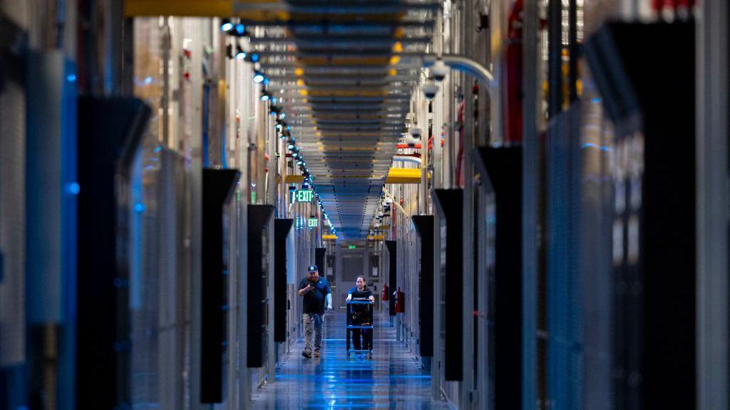 Two people pushing a trolley through a data centre 