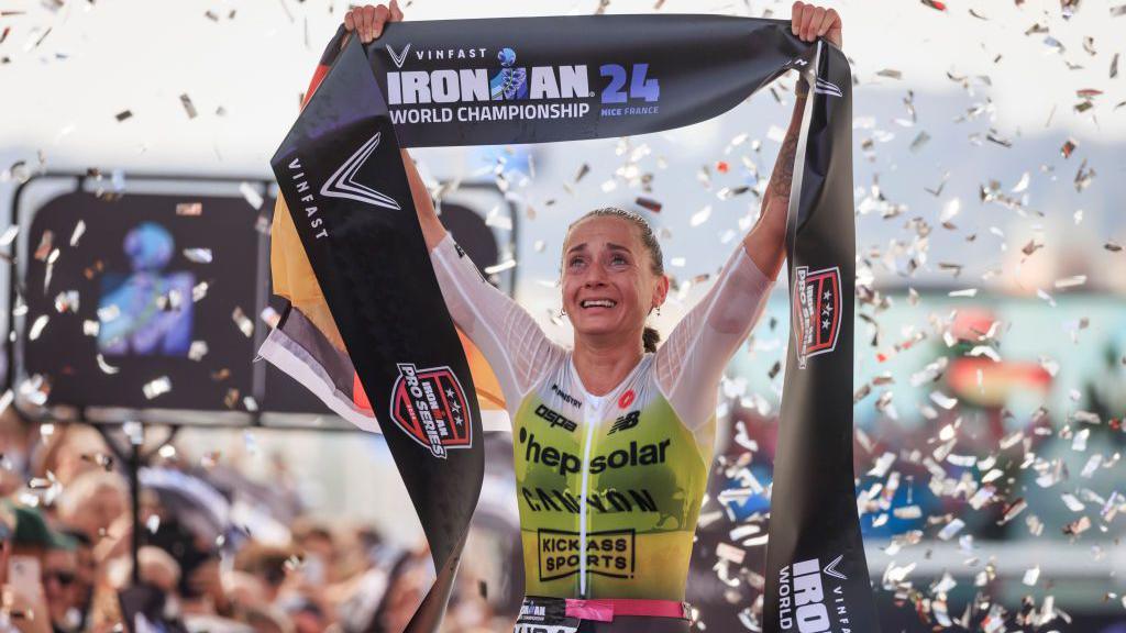 Laura Philipp holds aloft the finish line ribbon after winning the Ironman World Championship in Nice, France, as confetti falls around her