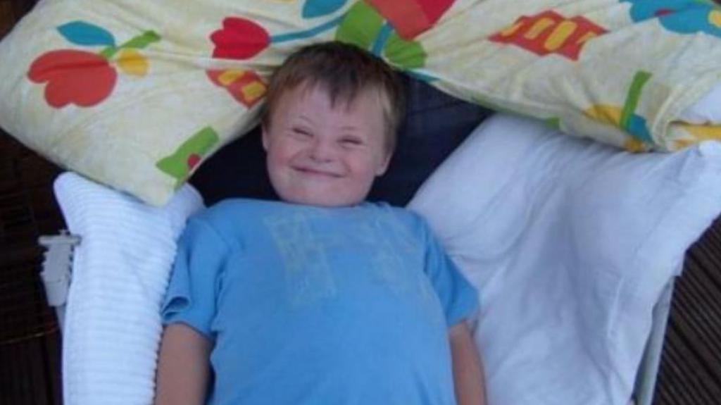 Joel as a young boy. He is lying on pillows and wearing a blue T-shirt