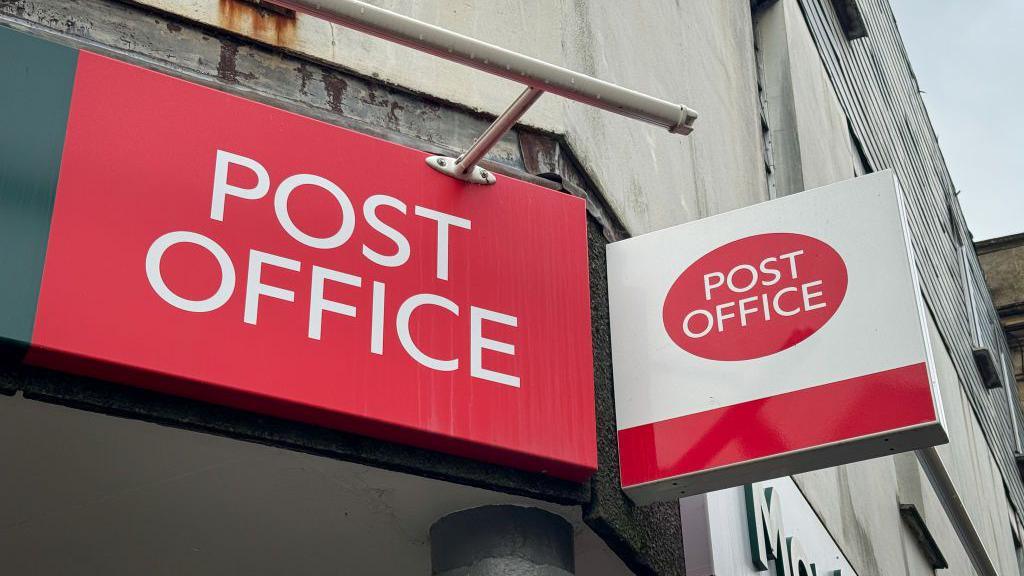 The logo of the Post Office is displayed in two red and white signs hung above a branch.