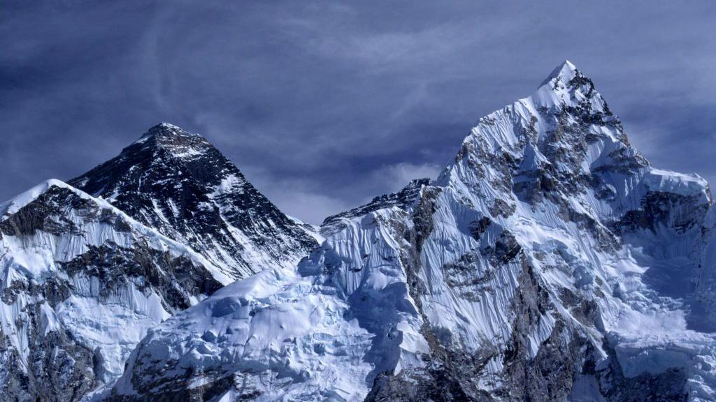 Mount Everest. Two mountain peaks covered in snow. The sky is dark blue and it looks stormy. 