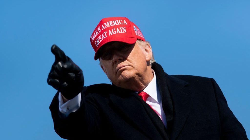 Donald Trump pointing while wearing a red cap which says "Make America great again"