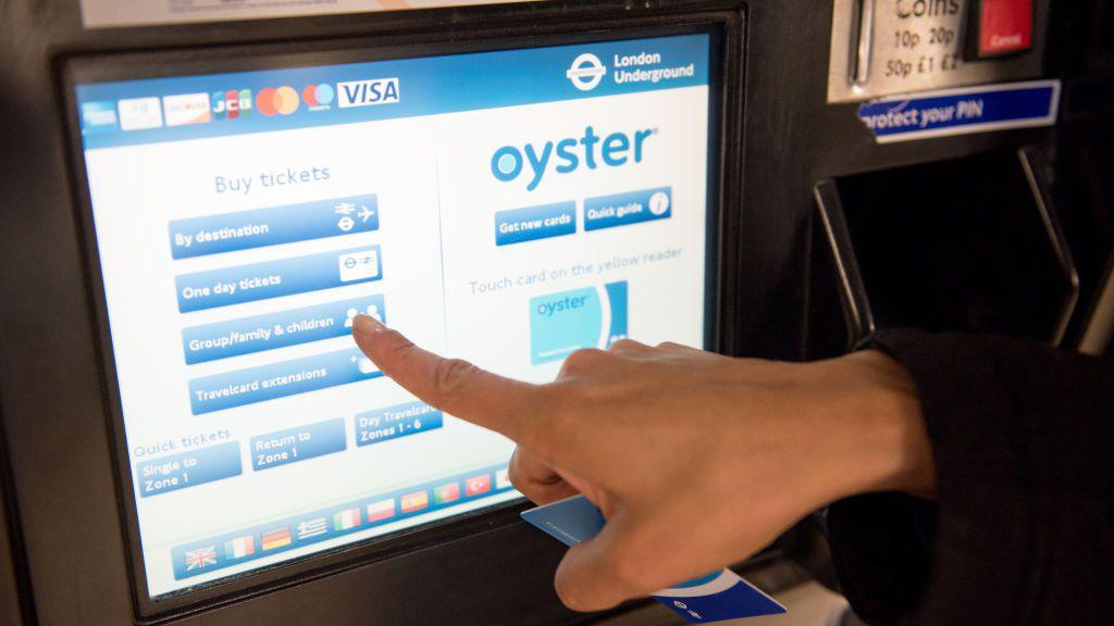 A commuter touches a touch screen Oyster ticket machine at an underground station