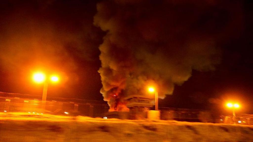 Large plumes of smoke rise from a structure with flames visible