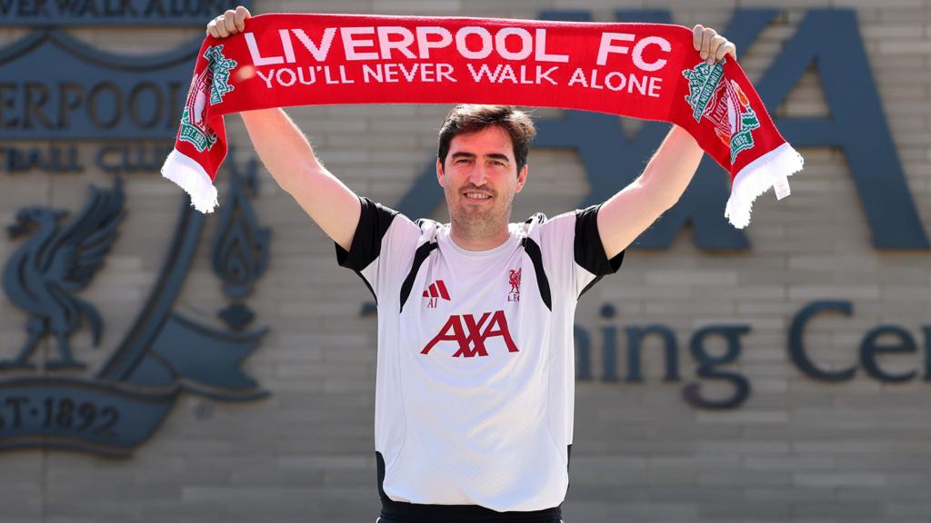 Andoni Iraola holds a Liverpool scarf with the words You'll Never Walk Alone above his head outside the club's training base
