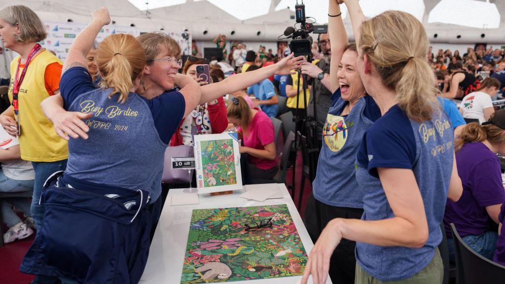 People celebrating winning the World Jigsaw Championships around a table 