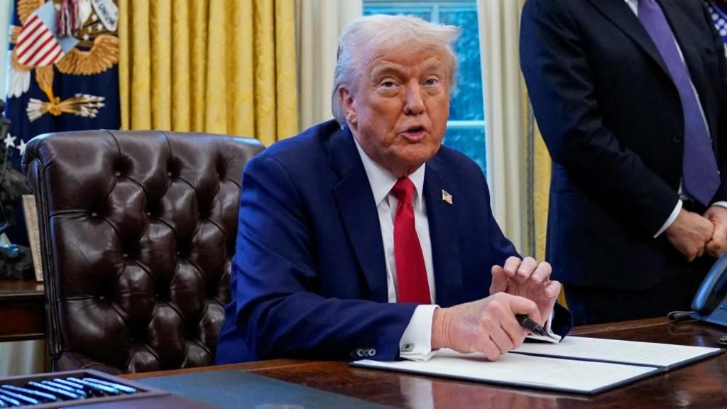 Trump speaks, sitting at his desk in the Oval Office