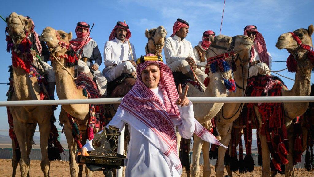 Tom Pidcock poses with a trophy, with camels behind him